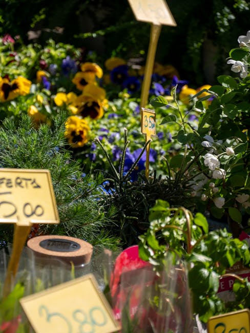 A vibrant display of freshly cut flowers arranged in a garden setting, featuring yellow and purple pansies, white flowering branches, and lush green foliage. The flowers are arranged in small clusters