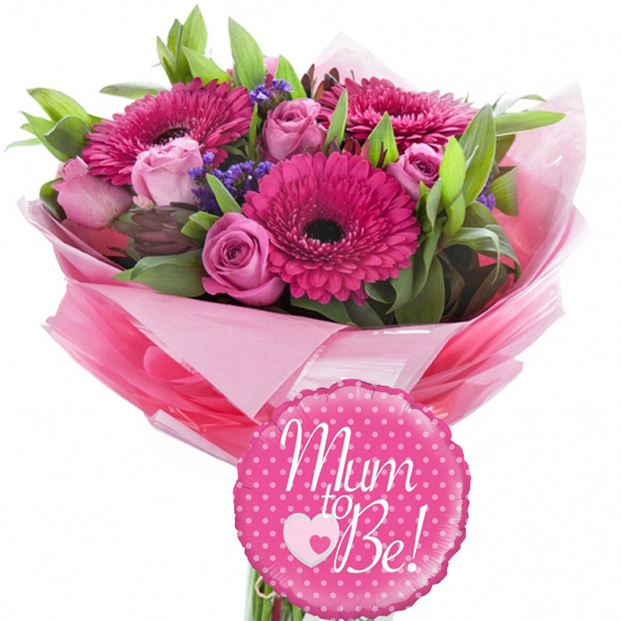 The photograph captures a celebratory Mum to Be floral arrangement on a seamless white background, giving the piece a crisp, contemporary feel reminiscent of a freshly decorated nursery in Kentish Town. Dominating the bouquet are several striking gerbera daisies in a bold fuchsia pink, the petals forming precise spokes around velvety dark centres that lend depth and drama. Nestled closely beside them are roses in varied shades of pink, from gentle pastel to mid-tone candy hues. Some roses are still tightly furled, their petals wrapping snugly around one another, while others are just beginning to open, offering glimpses of their intricate inner whorls. Tiny clusters of purple filler flowers, similar to statice, add a whisper of lavender colour that bridges the pinks and greens, and their small, papery blossoms contribute a light, cloud-like texture. Surrounding the blooms is a frame of green foliage, including narrow leaves that arch gracefully and broader, shinier leaves that catch the light, reinforcing the bouquet's rounded silhouette. The stems disappear into a voluminous wrapping of pink tissue paper layered in different tones, the edges crinkled and folded, creating a soft, almost fabric-like effect that feels especially feminine. Over this lies a sheath of clear, glossy cellophane that glints gently, highlighting the bouquet's status as a special gift. In front of the wrap sits a circular foil balloon, predominantly bright pink with a scalloped rim and sprinkled with evenly spaced white polka dots that evoke celebration. At the centre of the balloon, in flowing white cursive, is the phrase Mum to Be!, accented with a white heart outline sheltering a smaller solid pink heart. The overall composition expresses joyful anticipation, perfectly suited to be carried through the streets around Kelly Street or Inkerman Road to honour an expectant mother.