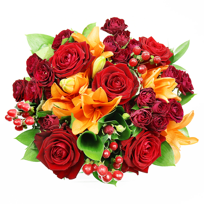 Captured from directly above on a stark white backdrop, this circular bouquet presents a rich tapestry of autumnal reds and warm oranges that feels simultaneously opulent and approachable. Prominent, fully opened deep red roses establish the bouquet's romantic heart-each velvet petal layered into a rosette that catches subtle variations of light and shadow. Bright Asiatic lilies in vivid orange are woven through the design; their trumpet-shaped petals and mid-toned speckling draw the eye, while visible stamens add a tactile, botanical honesty. Tightly packed spray roses in a deep wine hue nestle close to the larger blooms, bringing concentrated colour and a plush texture that deepens the visual field. Here and there, clusters of glossy Hypericum berries add small, reflective highlights-ruby spheres that feel almost jewel-like against the foliage. The arrangement's greens, broad and glossy like ruscus or salal, provide a fresh, cooling backdrop that makes the warm tones sing and helps define the bouquet's perfect roundness. The lighting is measured and gentle, designed to enhance petal translucency and the lilies' subtle sheen without creating harsh contrast. There is a faint, inviting aroma in the mind's nose: the classic, velvety scent of roses softened by the lilies' citrusy-spicy lift. As a floral piece suited to anniversaries, heartfelt congratulations, or an elegant autumnal table, this bouquet would travel well across Kentish Town and nearby Camden, offering a feeling of warmth, celebration, and considered craftsmanship.